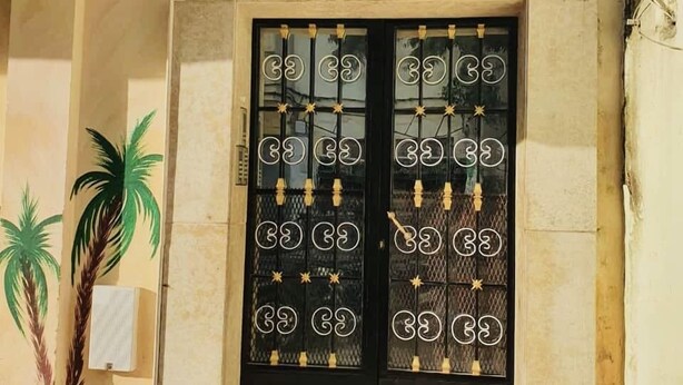 Una entrada de edificio con una puerta negra que tiene detalles de metal decorativo y un letrero encima.