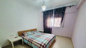 Un dormitorio con cama, mesita de noche, ventana con cortinas y candelabro.