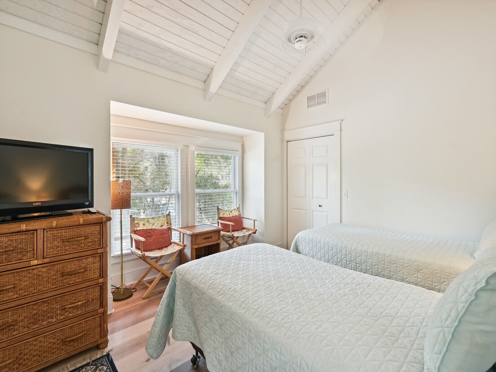 A bedroom with two beds, a television, a wicker dresser, and a window with blinds.