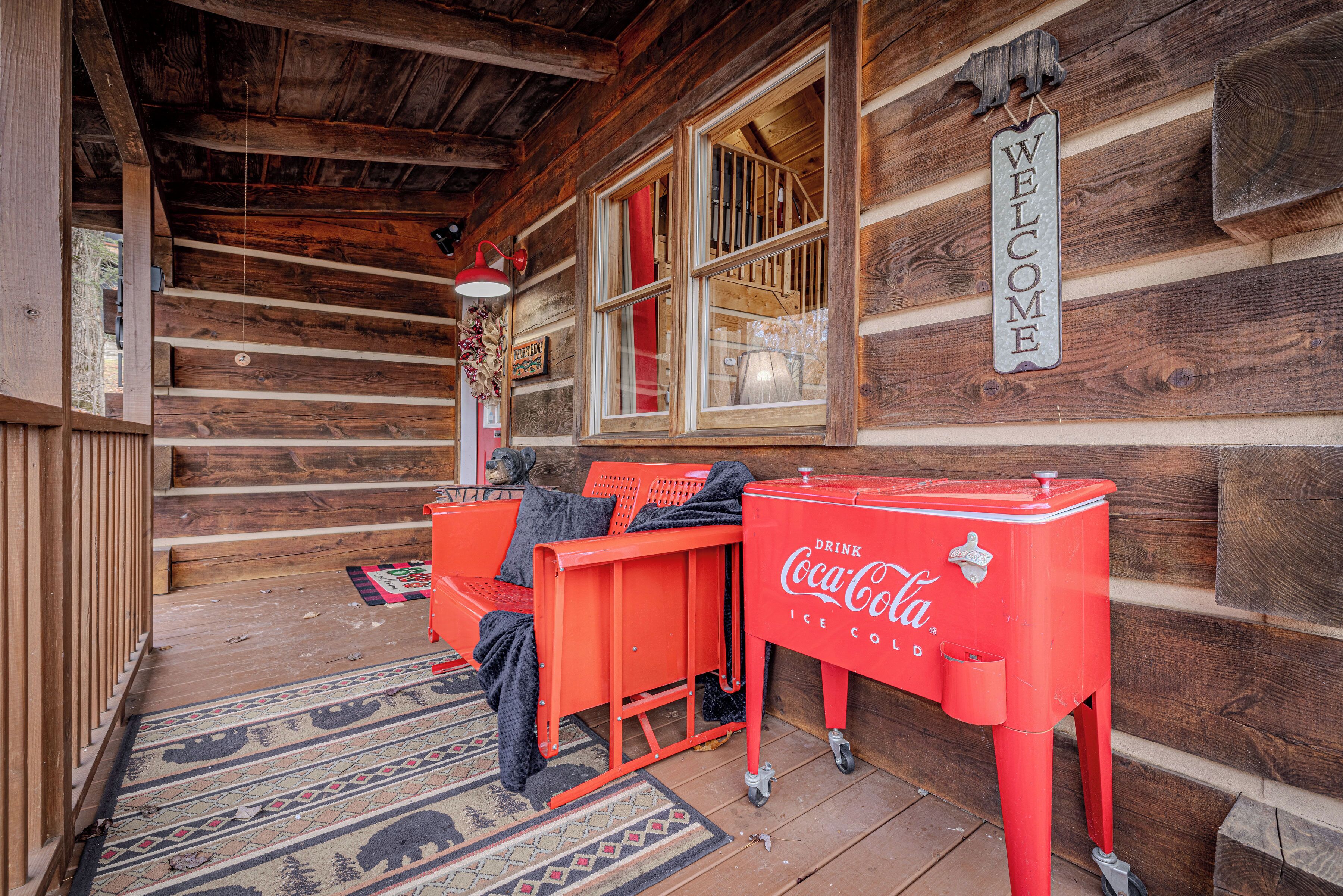 Una cabaña de madera con un enfriador rojo de Coca-Cola y un banco en el porche.