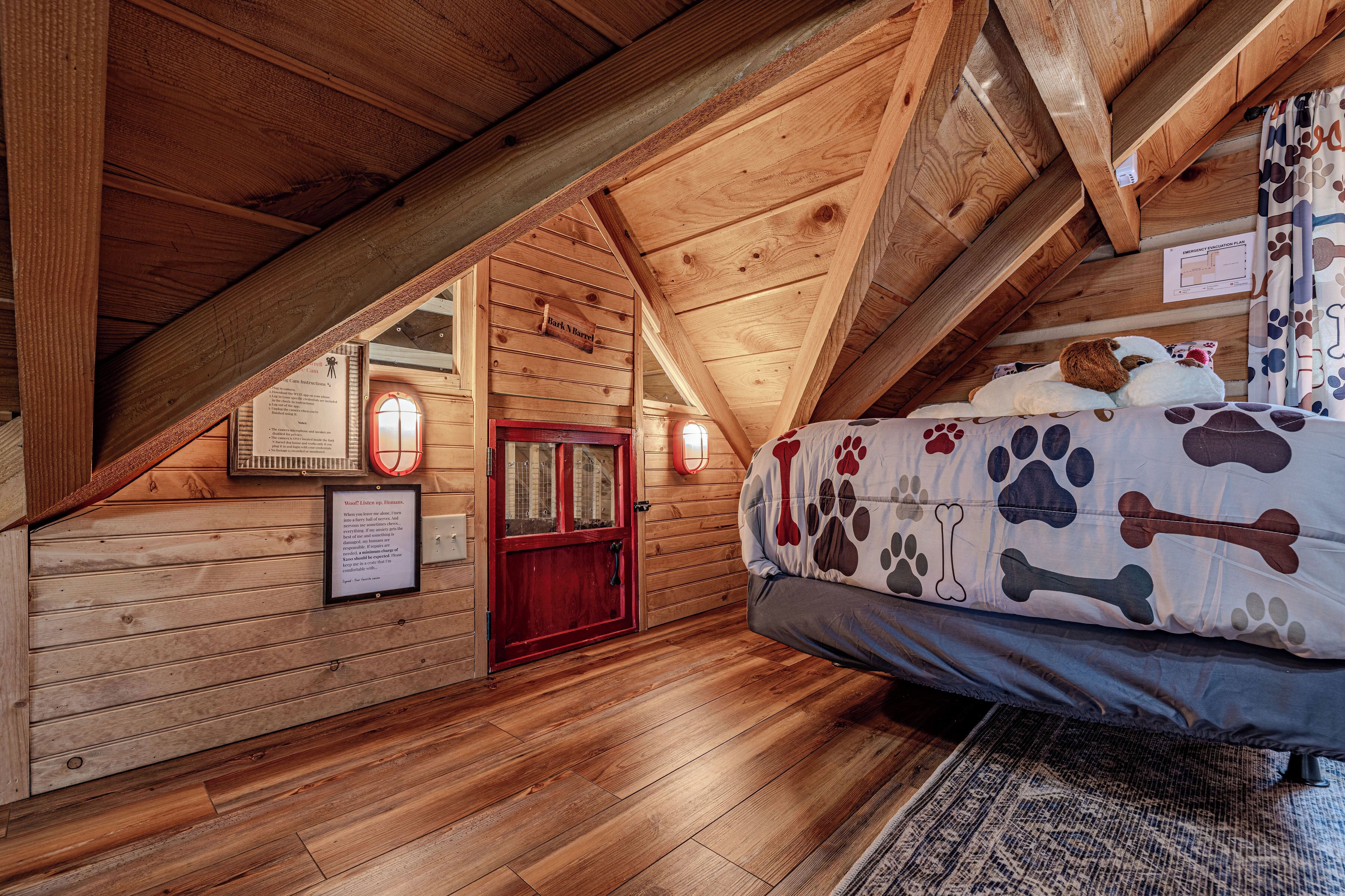 Un dormitorio de cabaña de madera con techo inclinado, una cama con manta de estampado hueso, una puerta roja y un cartel informativo enmarcado.
