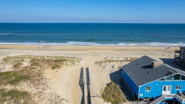 A beach house with a direct view of the ocean, a sandy beach, and a wooden boardwalk leading to the water.