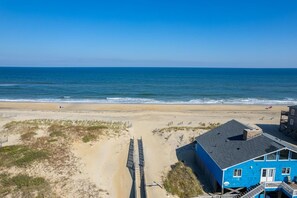 A beach house with a direct view of the ocean, a sandy beach, and a wooden boardwalk leading to the water.