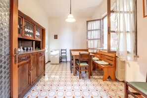 A kitchen with wooden cabinets, a refrigerator, a dining table with chairs, and a hanging light fixture.