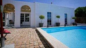 A modern house with a swimming pool, stone patio, and potted plants.