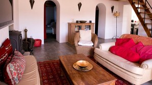 A spacious living area with a high wooden ceiling, a red hanging light fixture, and a staircase leading to an upper level.