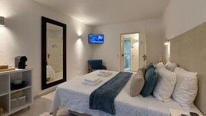 A hotel room with a bed, a TV mounted on the wall, a chair, and a shelf with a coffee maker.