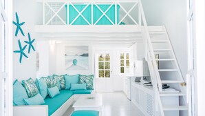 Un interior luminoso y blanco con un sofá color turquesa, una escalera blanca y vistas al exterior a través de una puerta.