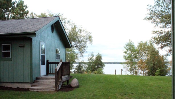 Una pequeña casa de un solo piso con porche y vista al lago.