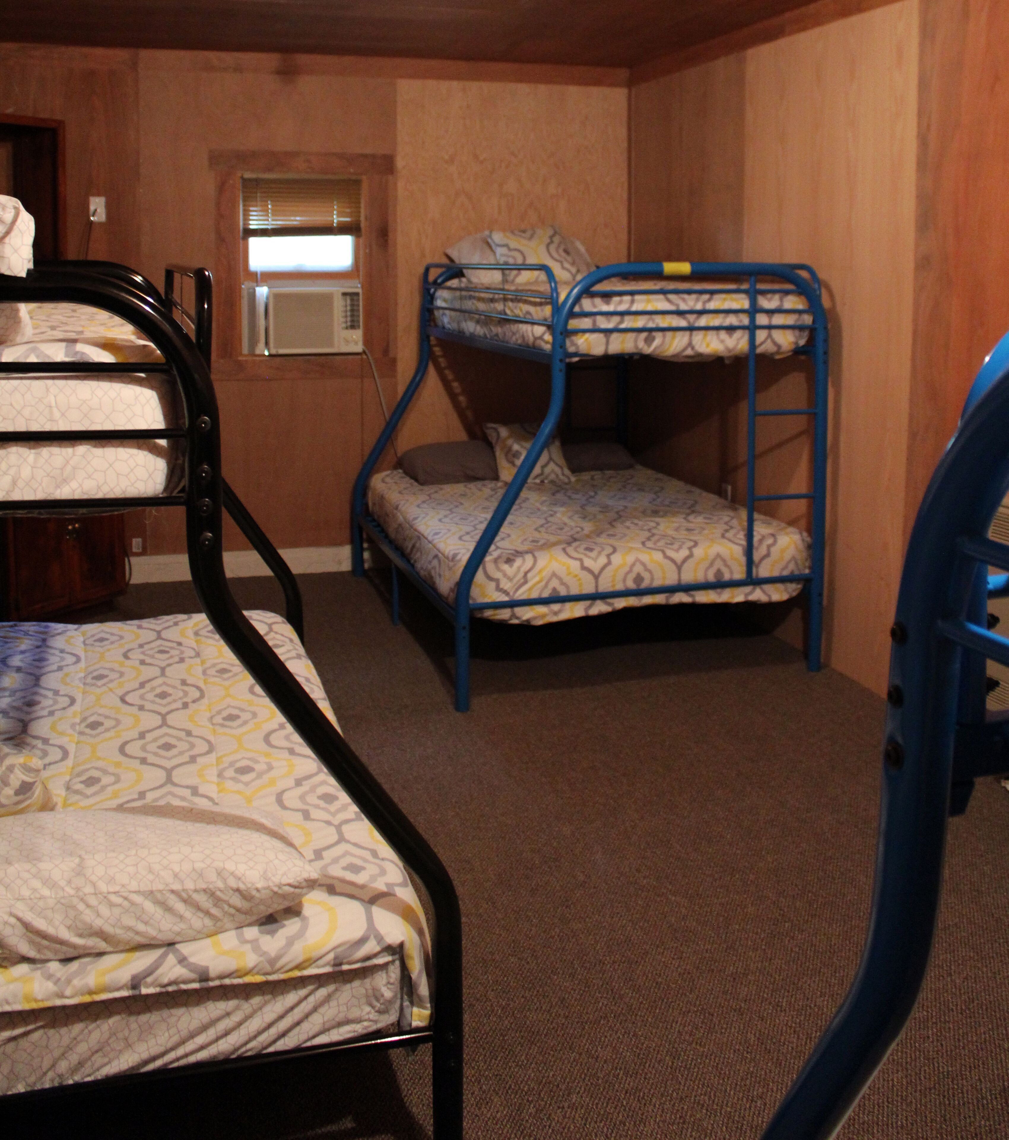 A room with bunk beds, a window with blinds, and a carpeted floor.