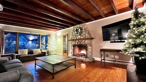 A cozy living room with a stone fireplace, a television mounted on the wall, and a Christmas tree.