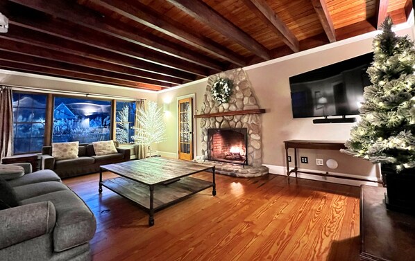 A cozy living room with a stone fireplace, a television mounted on the wall, and a Christmas tree. - Montauk Family Gem: HotTub, Pro Kitchen, Fireplace (Montauk)