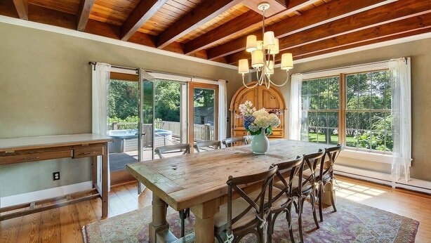 A spacious dining area with a wooden table and chairs, large windows, and a chandelier.