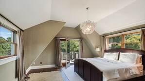 A bedroom with a large bed, a chandelier, and a view of the outdoors.