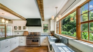 A modern kitchen with white cabinetry, a stainless steel stove, and large windows offering a view of greenery.