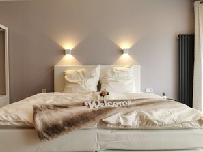 A neatly made bed with a 'Welcome' sign, two wall-mounted lights, and a small potted plant. - Modern apartment, private terrace, quiet location in the historic backyard (Henriettenhof)