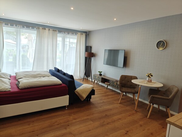 A modern hotel room with a bed, a sofa, a TV, a small table, and a chair. - Modern apartment, private terrace, quiet location in the historic backyard (Henriettenhof)