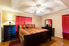 Ein Schlafzimmer mit Bett, Schminktisch, Nachttisch, Deckenventilator und roten Vorhängen.