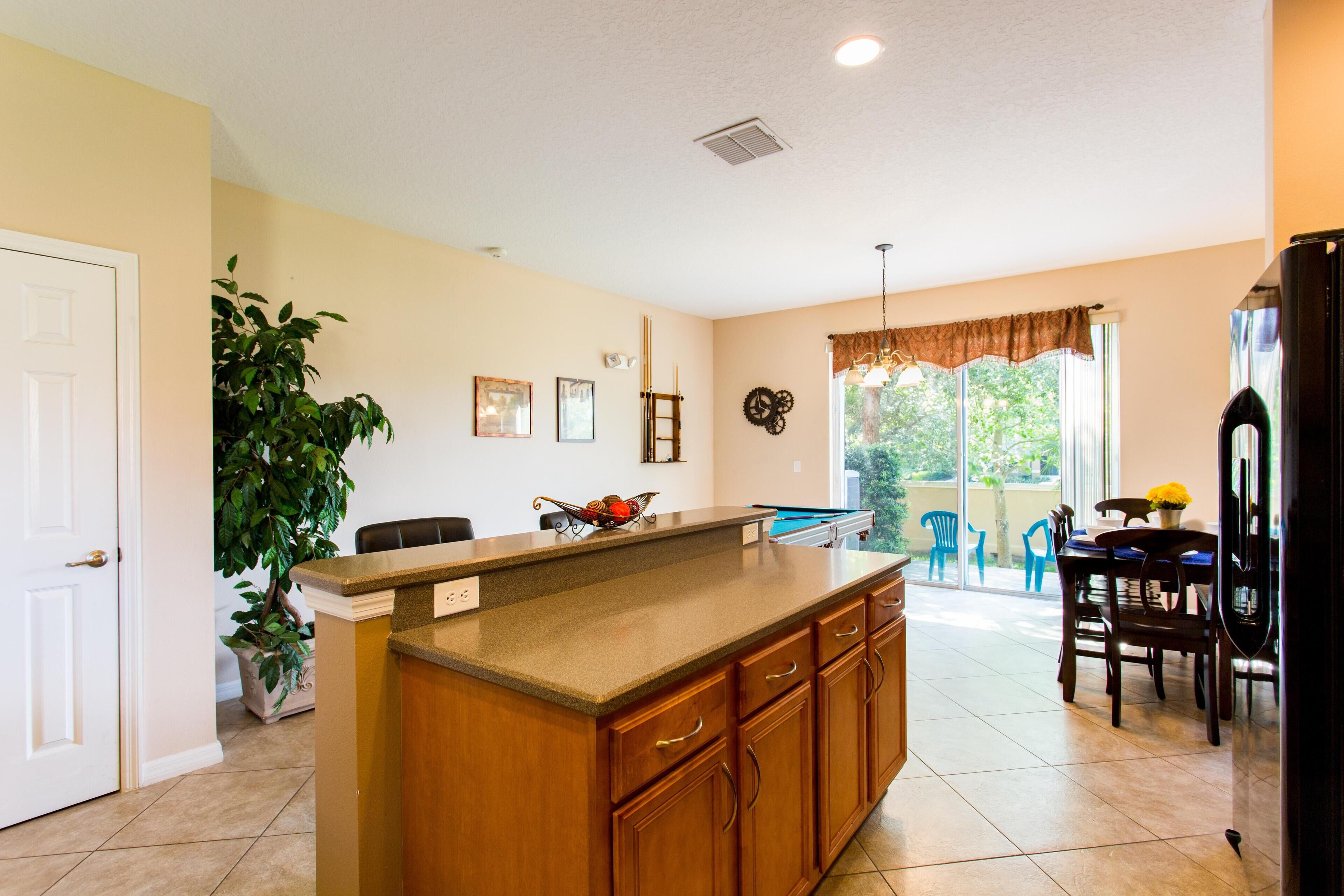 A kitchen with a large island, wooden cabinets, and a dining area with chairs and a table.