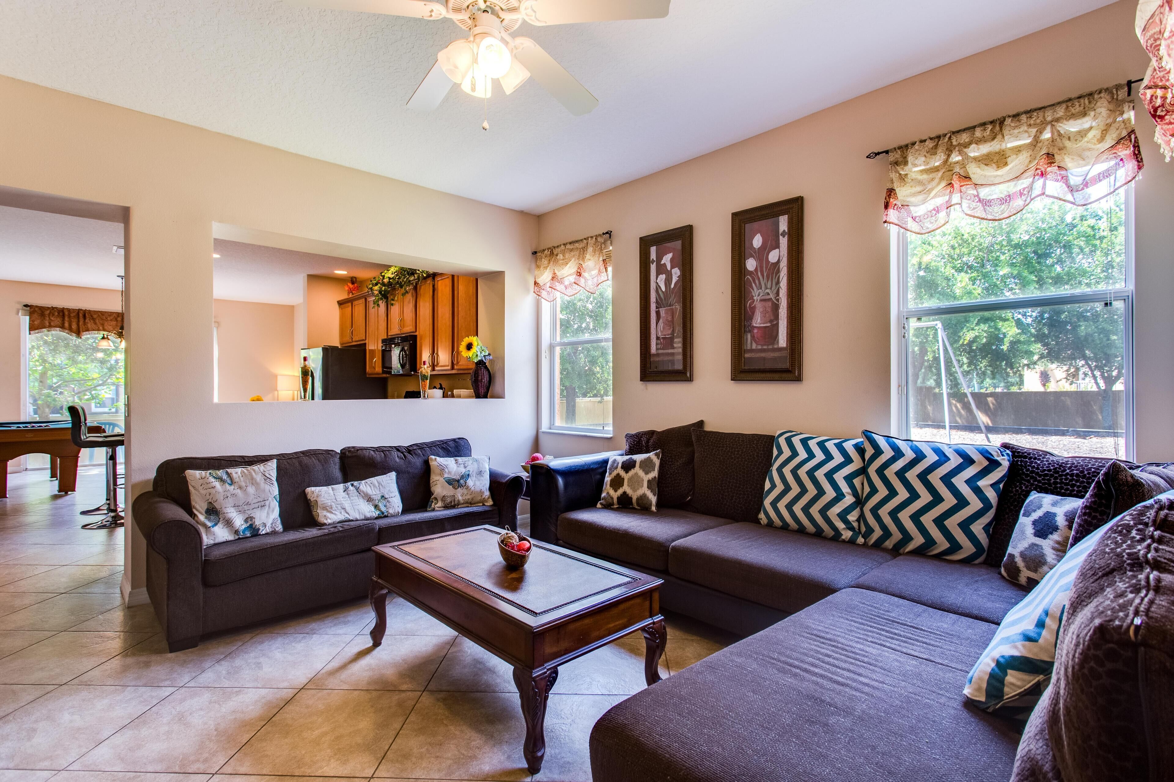 A spacious living room with a dark brown sofa set, a wooden coffee table, and a ceiling fan.