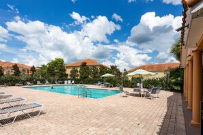 Ein Pool mit Liegestühlen und Sonnenschirmen, umgeben von Gebäuden mit roten Ziegeldächern.