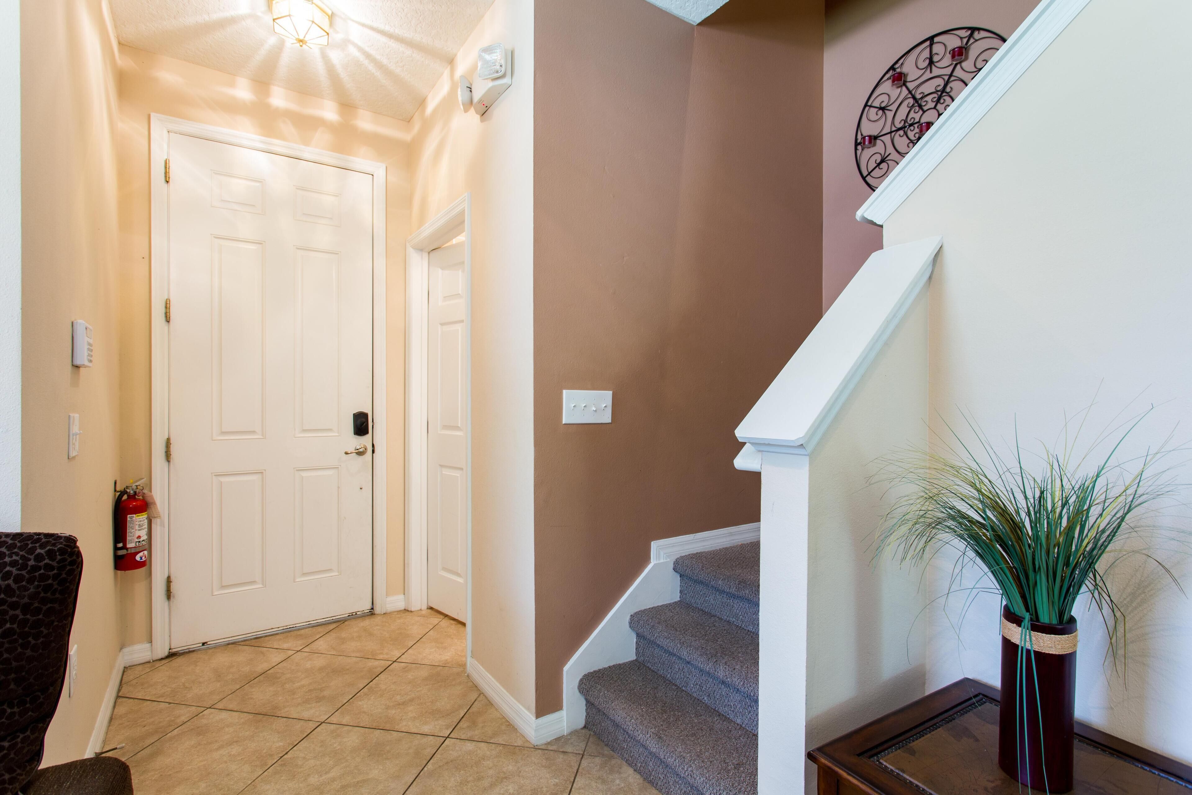 A hallway with a white door, a staircase, and a potted plant.