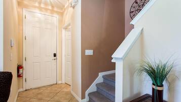 A hallway with a white door, a staircase, and a potted plant.
