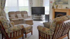 Een woonkamer met een bank, twee fauteuils, een televisie en een open haard.