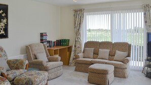 Een woonkamer met een zithoek, fauteuils, een tafeltje met boeken en een raam met gordijnen.