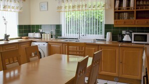 Een keuken met houten kastjes, een eettafel en een raam met gordijnen.