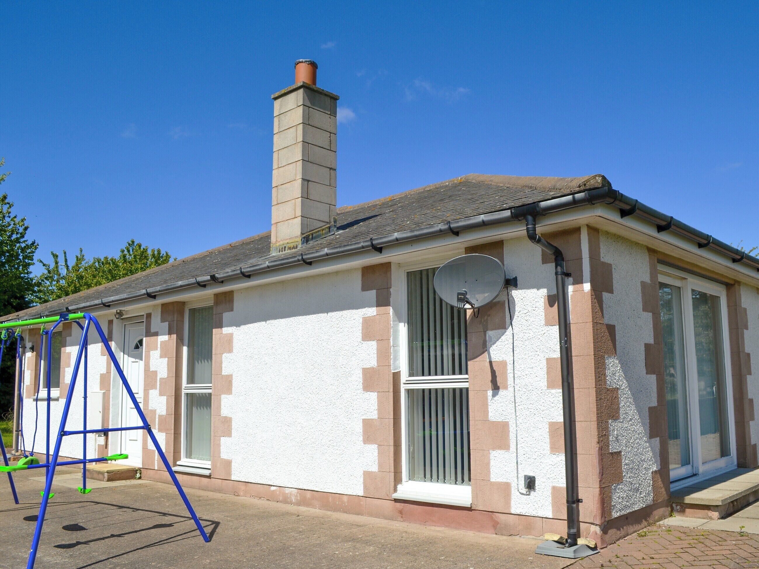A single-story building with a chimney, a satellite dish, and a swing set.