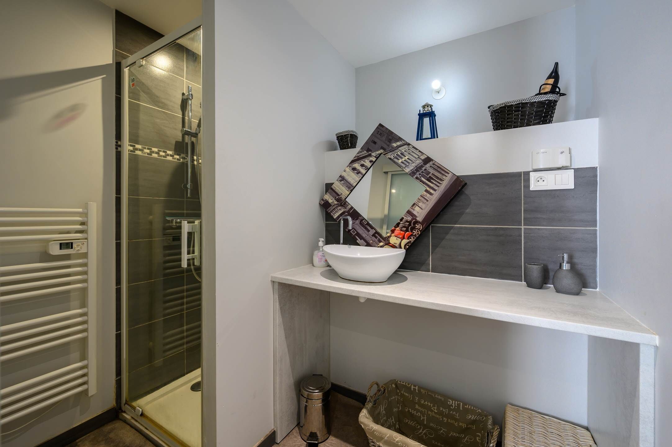 A bathroom with a glass shower enclosure, a white sink, and a mirror with a decorative frame.