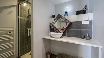 A bathroom with a glass shower enclosure, a white sink, and a mirror with a decorative frame.