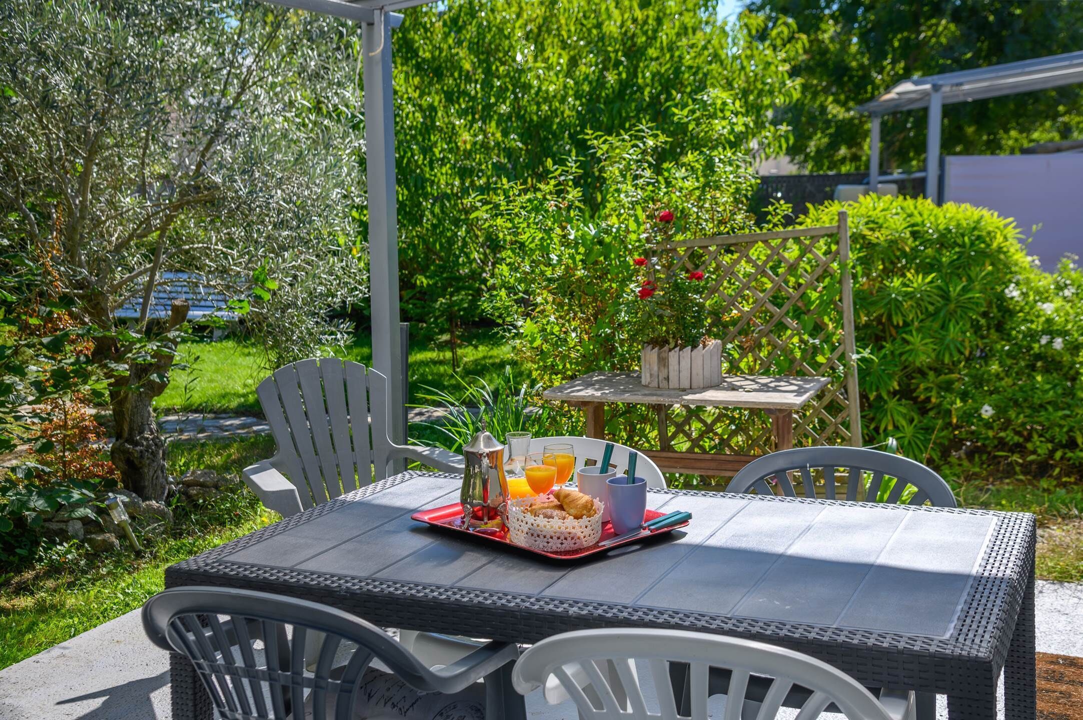 Un espace de restauration en plein air avec une table dressée pour le petit-déjeuner, entouré de verdure et agrémenté d’une pergola.