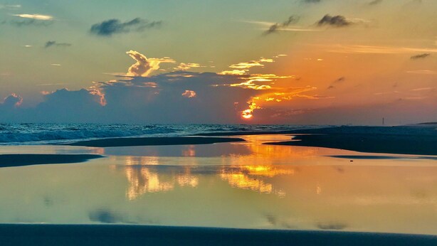 A beach with a sunset, calm water, and a distant lighthouse.