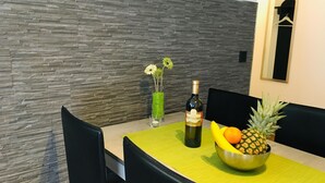 Une table à manger avec une bouteille de vin, un saladier de fruits et un vase rempli de fleurs.