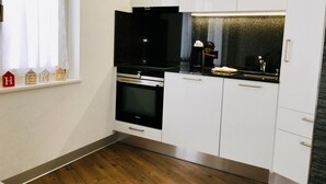 Une cuisine moderne avec des meubles blancs, une cuisinière noire et une fenêtre avec des rideaux.