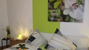 Une chambre à coucher bien rangée, avec un lit, des oreillers, une table de chevet avec une lampe, une petite plante en pot et un tableau encadré au mur.