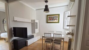 Una sala moderna con un sofá, un televisor, una mesa de comedor con sillas y un cuadro en la pared.