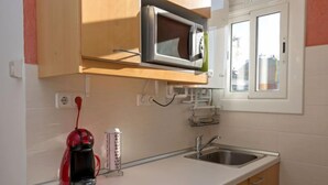 Una cocina con microondas, cafetera, lavamanos y ventana.