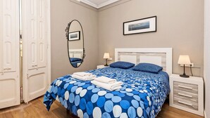 Un dormitorio con cama, dos mesitas de noche, un tocador, un espejo y un cuadro enmarcado en la pared.