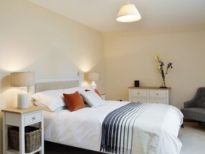 A neatly arranged bedroom with a bed, bedside tables, a lamp, a vase with flowers, and a chair. - The Stables - UK11108 (Montrose)