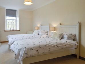 A double bed with a white and black pattern, two bedside tables with lamps, a window with a blind, and a white headboard. - The Stables - UK11108 (Montrose)
