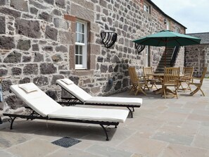 A stone building with a stone wall, a window, a table with chairs, and a sunbed. - The Stables - UK11108 (Montrose)