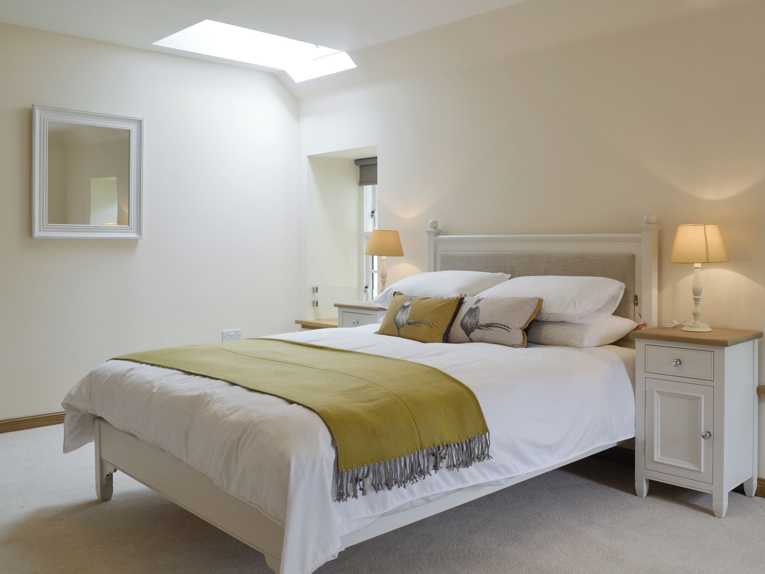 Une chambre à coucher avec un lit, des tables de chevet, une commode, un miroir et une fenêtre de toit.