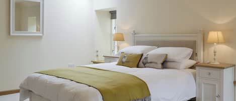 Un dormitorio con cama, mesitas de noche, un tocador, un espejo y un tragaluz.