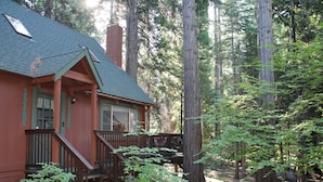 A cabin with a wooden deck, surrounded by tall trees.