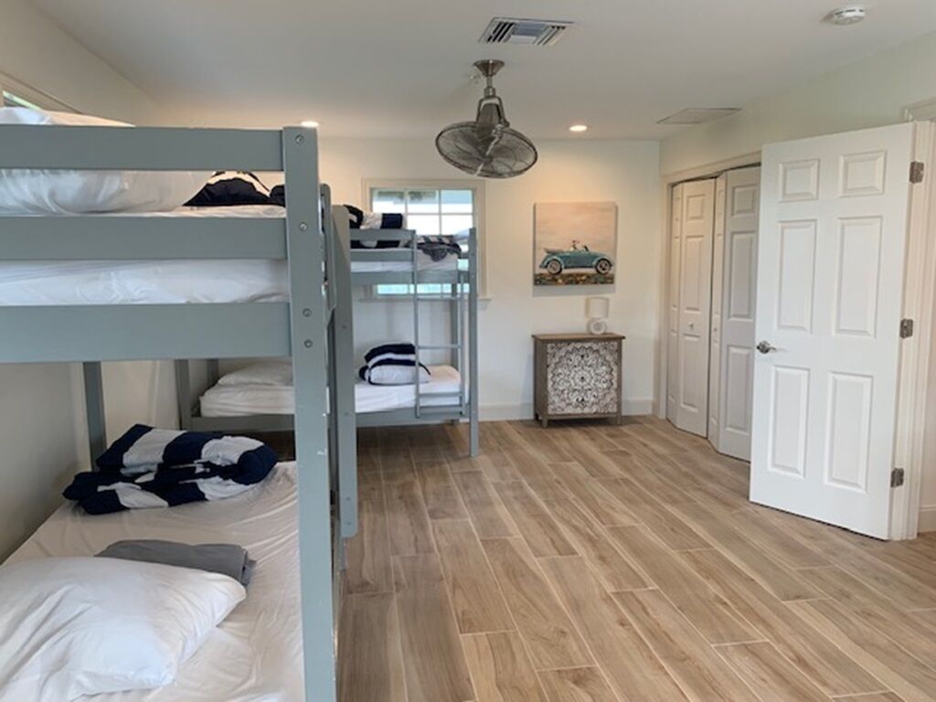 Une chambre avec un lit superposé, un ventilateur de plafond, une porte et une petite table sur laquelle est posé un objet décoratif.