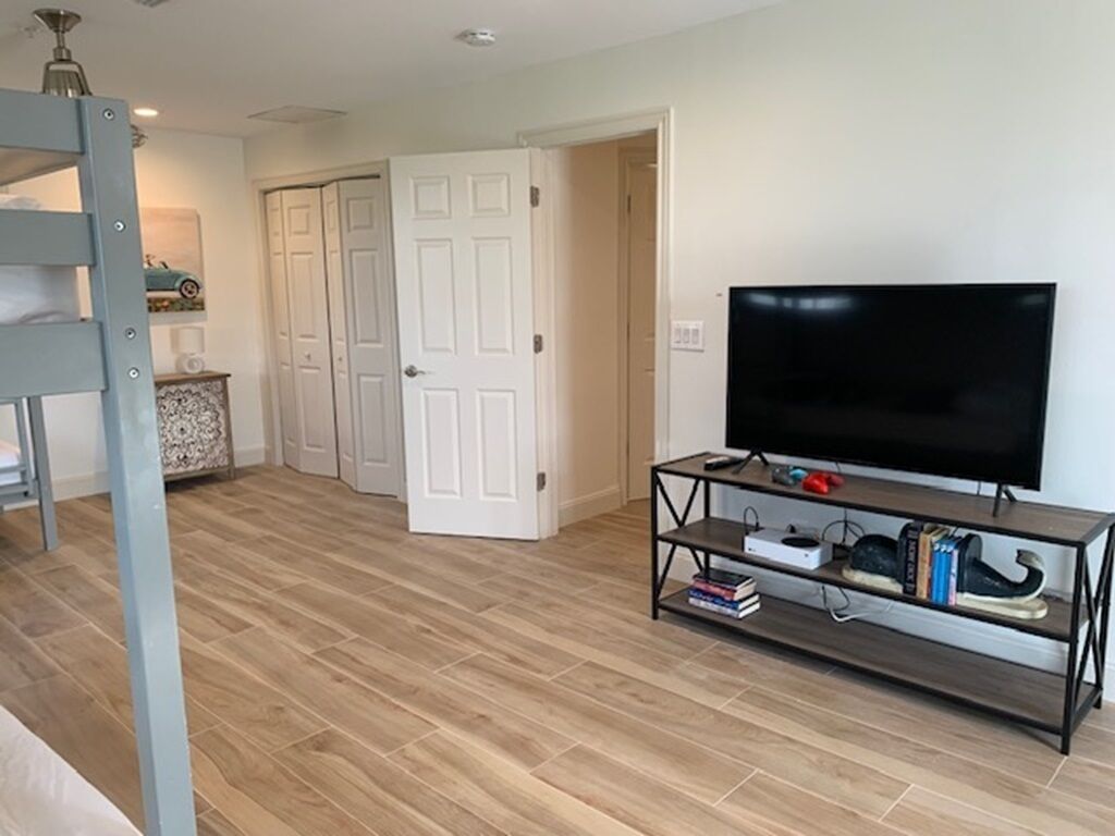 Una sala de estar con un televisor sobre un mueble bajo, una cama litera y una puerta que da a otra habitación.