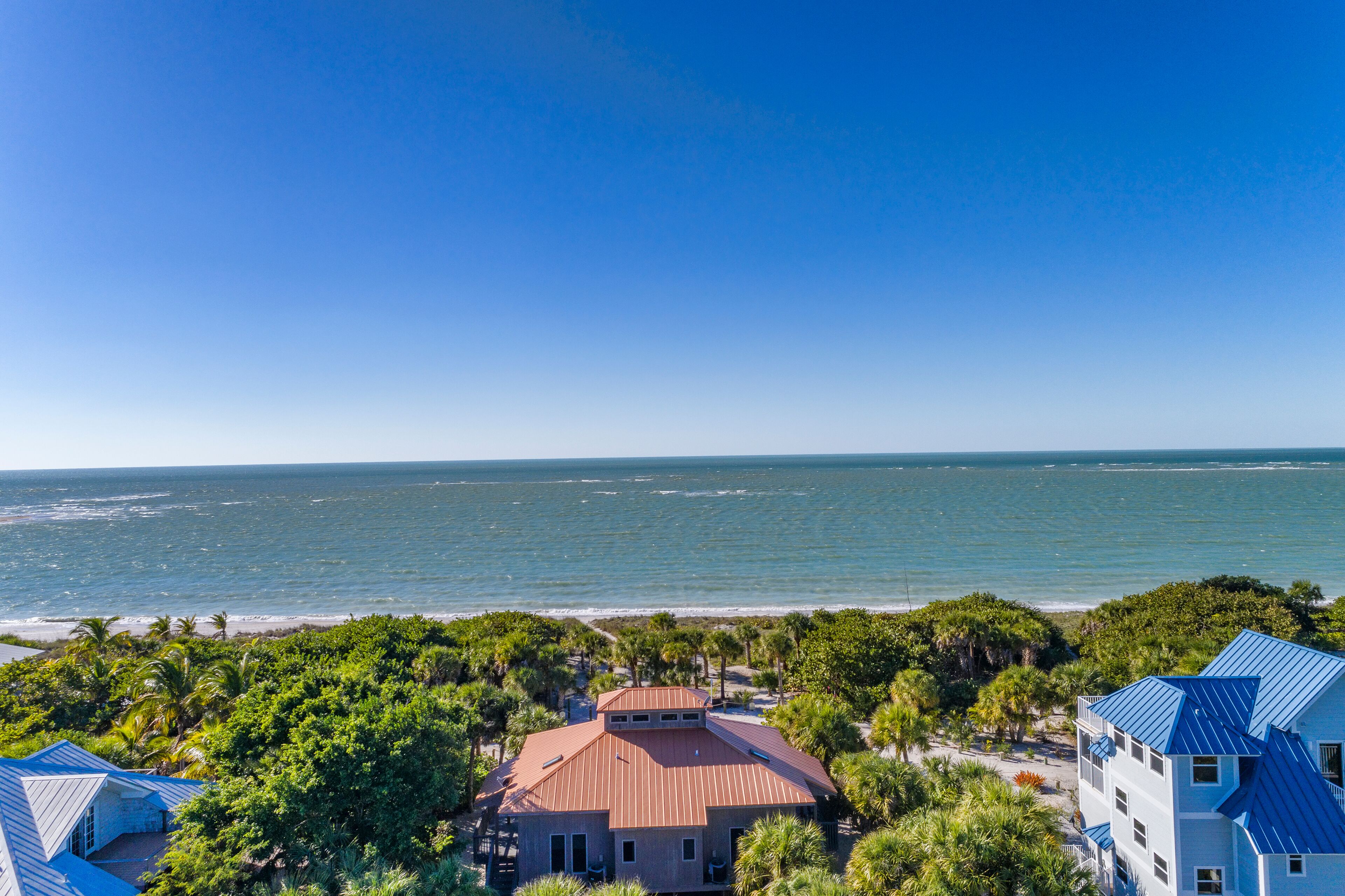 A coastal property with a large house featuring a red roof, surrounded by lush greenery and a view of the ocean.